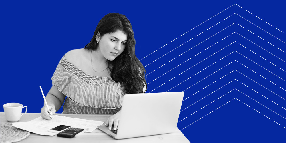 A woman sitting at a table with her laptop, pen and paper, and a calculator